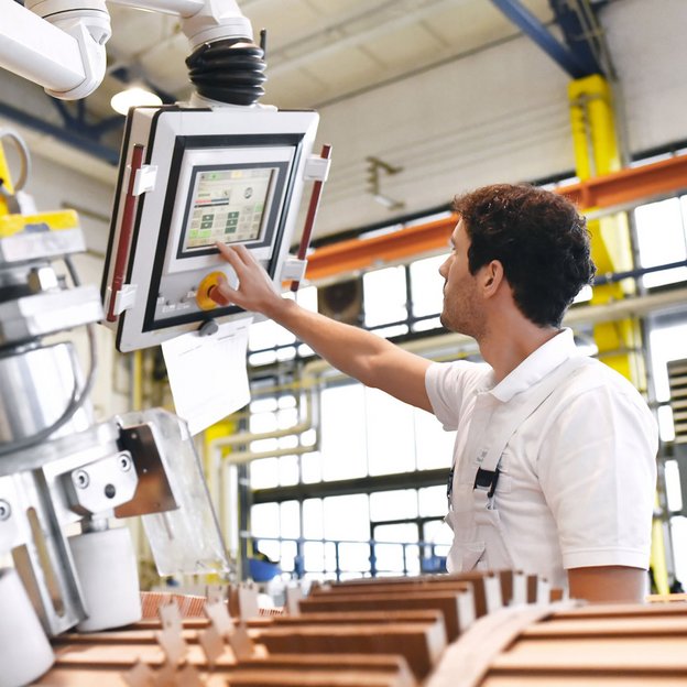 Mitarbeiter bedient ein Steuerungspanel an einer Industrieanlage in moderner Produktionshalle.