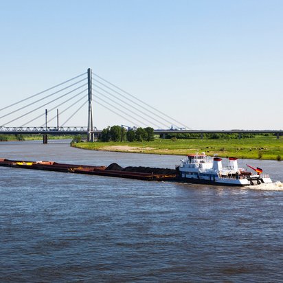 Frachtschiff auf dem Rhein bei Wesel mit Blick auf die Rheinbrücke und grüne Uferlandschaft