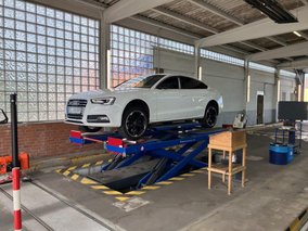 Weißer Audi auf einer Hebebühne in der TÜV NORD Station Geldern während einer Fahrzeuguntersuchung.