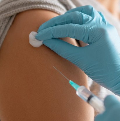 Person mit Maske erhält Injektion in den Oberarm durch medizinisches Fachpersonal mit Handschuhen.