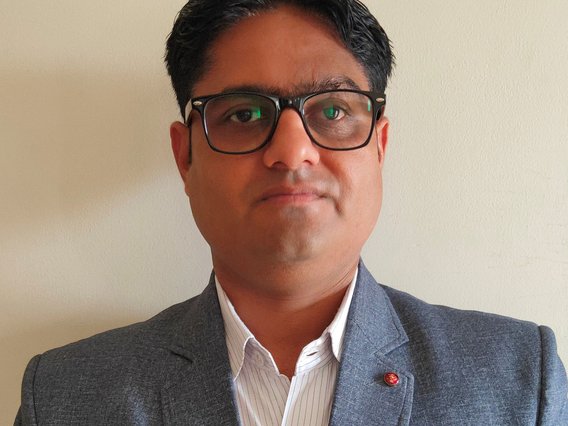 Porträtaufnahme von Jayesh Patal mit Brille in grauem Anzug und gestreiftem Hemd vor einer hellen Wand.