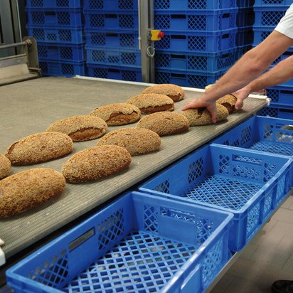 Symbolbild ISO 22000 Zertifizierung - Hände eines Mitarbeitenden greifen Brote von einem Laufban