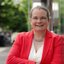 Doreen Kirmse lächelt vor einem modernen Gebäude und trägt ein rotes Blazer.
