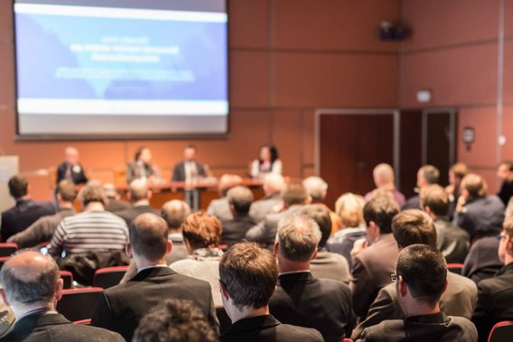 Blick in den Konferenzsaal mit Teilnehmenden und Podiumsdiskussion beim Symposium zur Lagerung und zum Transport radioaktiver Stoffe.