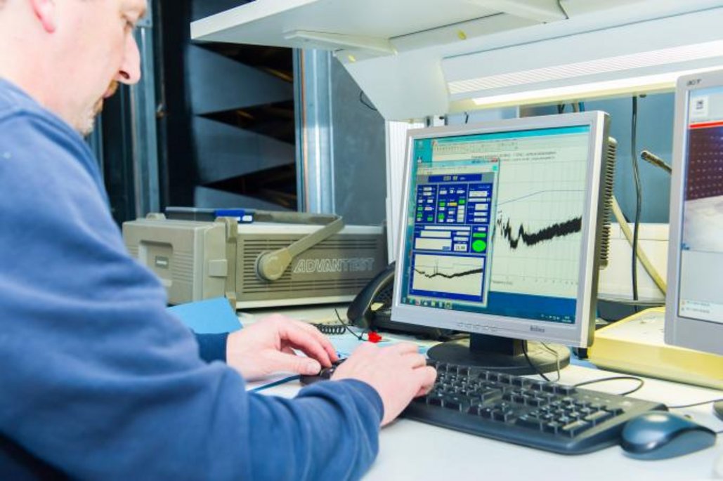 Techniker arbeitet an einem Computer und analysiert Messdaten mit spezieller Software in einem Testlabor.