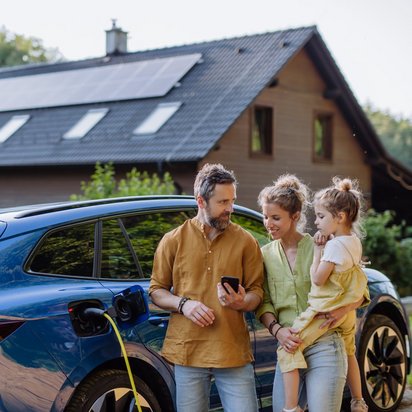 Familie lädt Elektroauto vor einem Haus mit Solaranlage