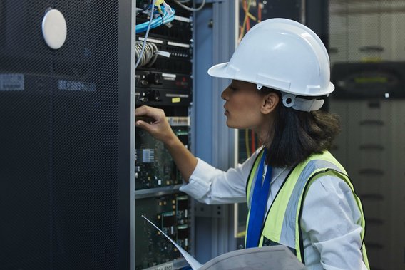 Technikerin mit Helm prüft Serverkomponenten in einem Rechenzentrum.