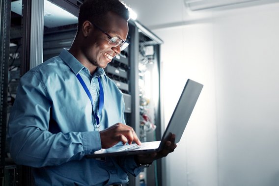 IT-Spezialist arbeitet mit Laptop im Serverraum und prüft Netzwerksysteme