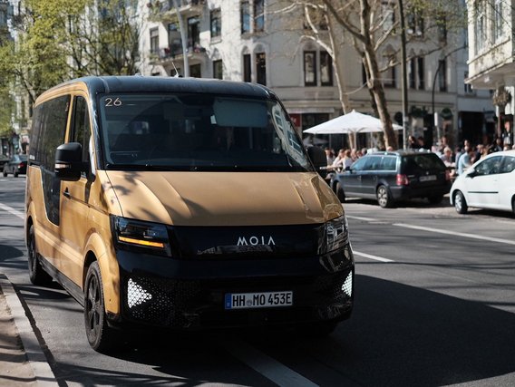 Goldener MOIA-Elektrobus mit schwarzen Akzenten auf einer Hamburger Straße mit historischen Gebäuden im Hintergrund.