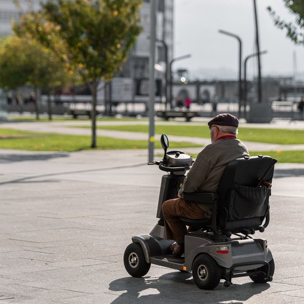 Älterer Mann fährt mit einem Elektrorollstuhl über einen sonnigen Platz in der Stadt