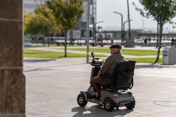 Älterer Mann fährt mit einem Elektrorollstuhl über einen sonnigen Platz in der Stadt