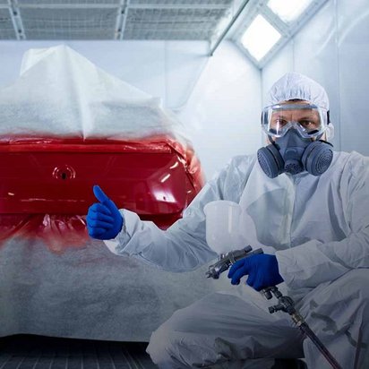 Fahrzeuglackierer in Schutzkleidung bei der Arbeit in einer Lackierkabine, rotes Auto wird lackiert