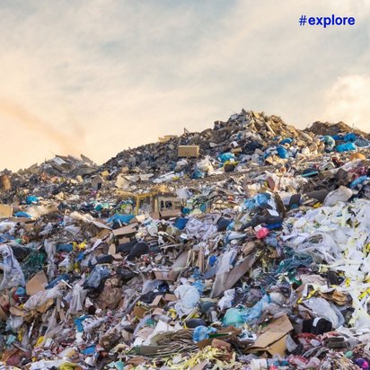 Große Mülldeponie mit verschiedenfarbigen Abfällen und einem Planierraupe im Hintergrund unter einem bewölkten Himmel bei Sonnenuntergang.