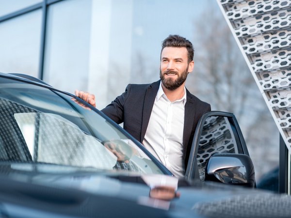 Mann im Anzug steigt lächelnd aus einem schwarzen Auto vor einem modernen Gebäude