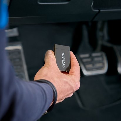 TÜV NORD Onboard Diagnose in einer Hand vor den Pedalen eines Autos