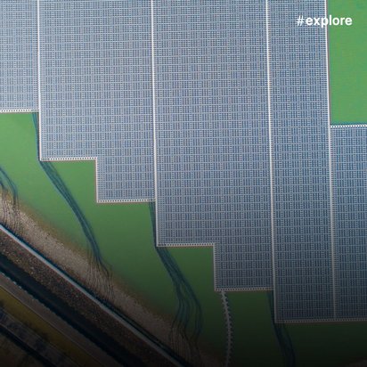 Nahaufnahme einer schwimmenden Solaranlage mit zackigem Rand. Die Anlage schwimmt auf grünlichem Wasser, links verläuft eine Straße am Ufer.