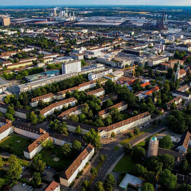 Luftaufnahme eines Stadtgebiets mit Industrie- und Wohnbebauung im Hintergrund