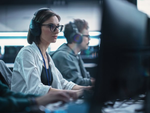 Personen arbeiten konzentriert an Computern in einem modernen Büro, tragen Headsets.