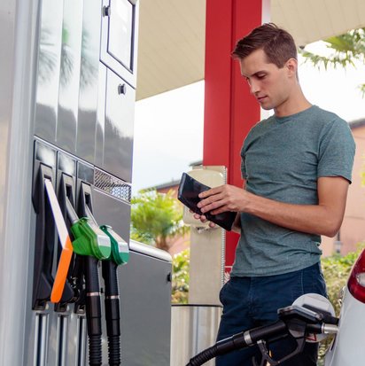Mann steht neben seinem Auto an der Tankstelle