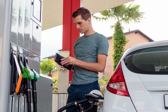 Mann steht neben seinem Auto an der Tankstelle