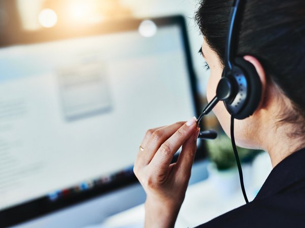 Frau mit Headset spricht vor einem Computerbildschirm im Kundenservice