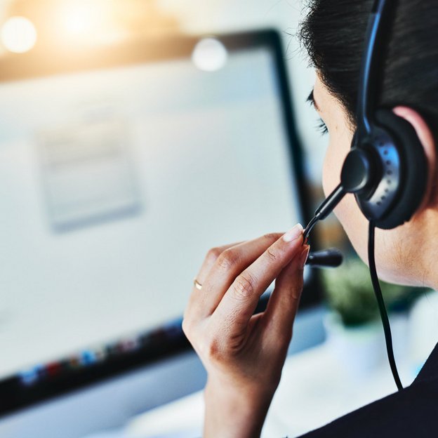 Frau mit Headset spricht vor einem Computerbildschirm im Kundenservice