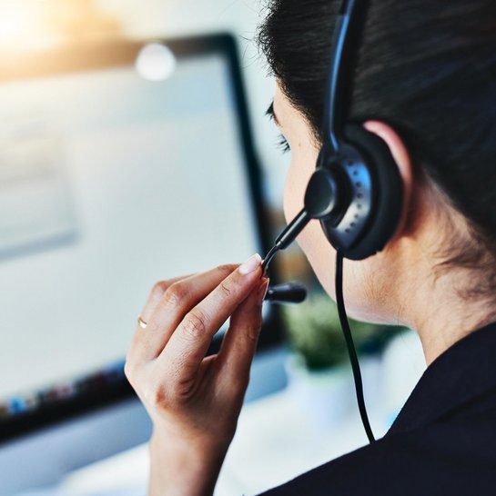 Frau mit Headset spricht vor einem Computerbildschirm im Kundenservice