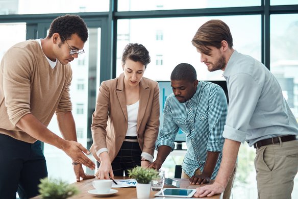 Vier Personen diskutieren konzentriert über Unterlagen auf einem Konferenztisch in einem modernen Büro.