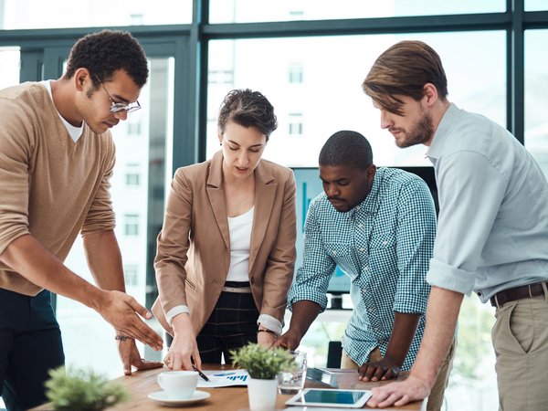 Vier Personen diskutieren konzentriert über Unterlagen auf einem Konferenztisch in einem modernen Büro.