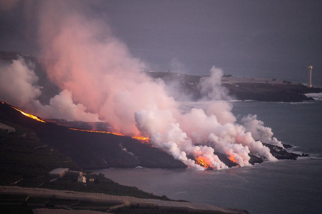 Ein aktiver Vulkanausbruch am Meer mit glühend roter Lava, die ins Wasser fließt und dabei massive weiße und rosa Dampfwolken erzeugt. Die dramatische Szene zeigt den Kontrast zwischen dem feurigen Lavastrom und dem dunklen Ozean bei Dämmerung.