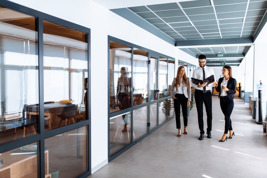 Personen sprechen und schauen sich Dokumente an, während sie den Büroflur entlang gehen