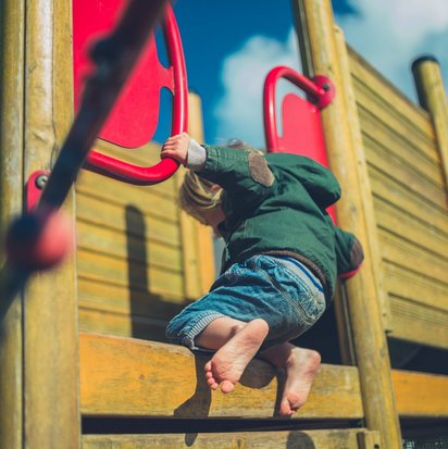 Ein Kind klettert barfuß auf ein Spielgerät.
