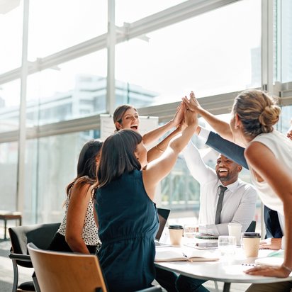Fünf Mitarbeitende der TÜV NORD Business Unit People and Empowerment stehen an einem Tisch und geben sich ein High-Five.