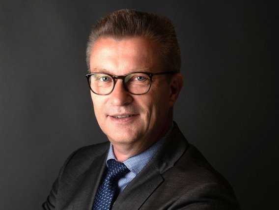 Jens Groffmann mit Brille und grauem Anzug vor dunklem Hintergrund.