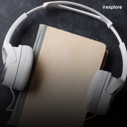 Weiße Over-Ear-Kopfhörer sind um ein geschlossenes Buch mit hellem Einband gelegt und ruhen auf einer dunklen, strukturierten Oberfläche. Die Szene suggeriert das Konzept von Hörbüchern oder Audio-Lerninhalten.