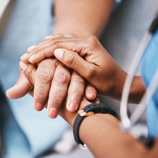 Pflegekraft hält tröstend die Hände einer älteren Person in einer einfühlsamen Geste.