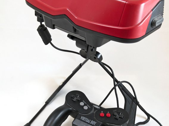Ein roter Virtual Boy von Nintendo auf einem Stativ, mit schwarzem Controller davor. Das VR-Headset aus den 1990ern war für monochrome 3D-Spiele konzipiert.