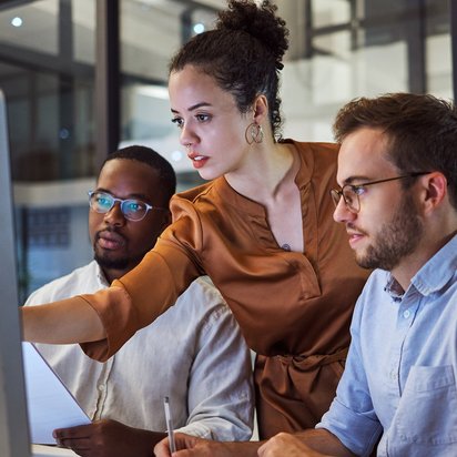 Teamleiter (TÜV) Eine Teamleiterin zeigt ihren Angestellten etwas auf dem Computer.