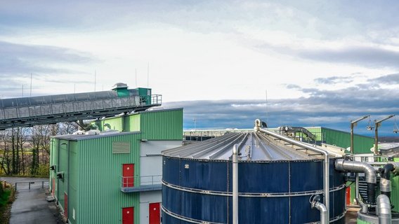 Industrielle Anlage mit grünen Gebäuden, großen Fermentern und Rohrleitungen, vermutlich Teil einer Biogas- oder Energieerzeugungsanlage.