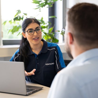Bautechnik-Kaufberatung Eine TÜV-NORD-Mitarbeiterin im Gespräch mit einem Kunden am Schreibtisch, ein Laptop steht vor ihr.