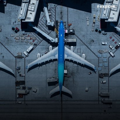  Luftaufnahme eines Flughafens mit drei Passagierflugzeugen an Gates - das mittlere Flugzeug ist auffällig blau lackiert, während die anderen beiden weiß sind.