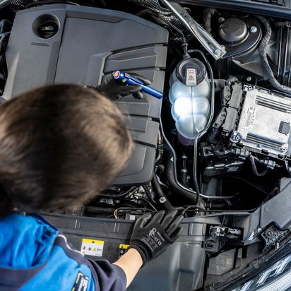 Mitarbeiterin von TÜV NORD beugt sich über eine geöffnete Motorhaube