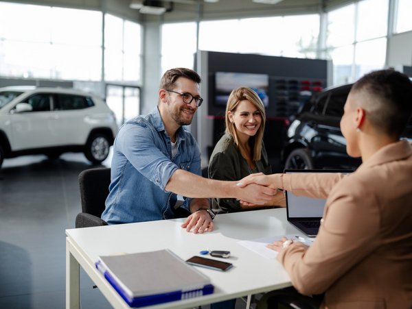 Kunden und Verkaufsberater geben sich im Autohaus die Hand, Autos im Hintergrund, Vertragsabschluss oder Beratungsgespräch.