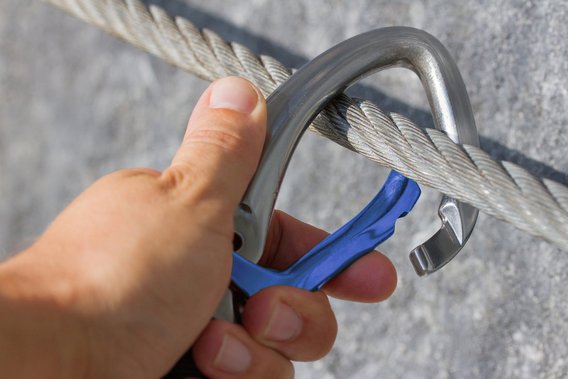 Nahaufnahme eines Karabiners, der an einem Drahtseil befestigt ist.