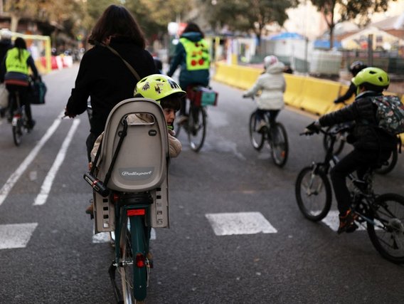 Gruppe von Radfahrern auf abgesichertem Fahrradweg mit gelben Begrenzungen; ein Kind mit Helm in Kindersitz auf dem Fahrrad einer Erwachsenen.