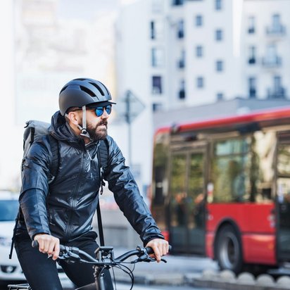 Fahrradfahrer mit Helm in der Stadt neben einem roten Bus