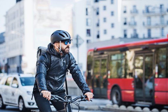 Fahrradfahrer mit Helm in der Stadt neben einem roten Bus