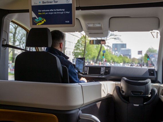 Innenansicht eines modernen Shuttlebusses mit beige-grauen Sitzen und einem Display, das "Berliner Tor" anzeigt.