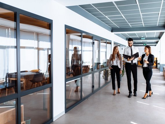 Personen sprechen und schauen sich Dokumente an, während sie den Büroflur entlang gehen