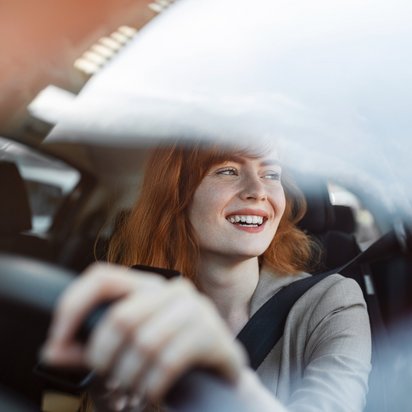Frau fährt ein Auto, Hände am Lenkrad, durch die Windschutzscheibe gesehen.